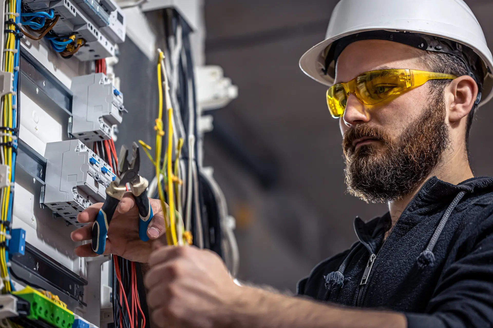 An electrician in safety glasses working inside an open switchboard