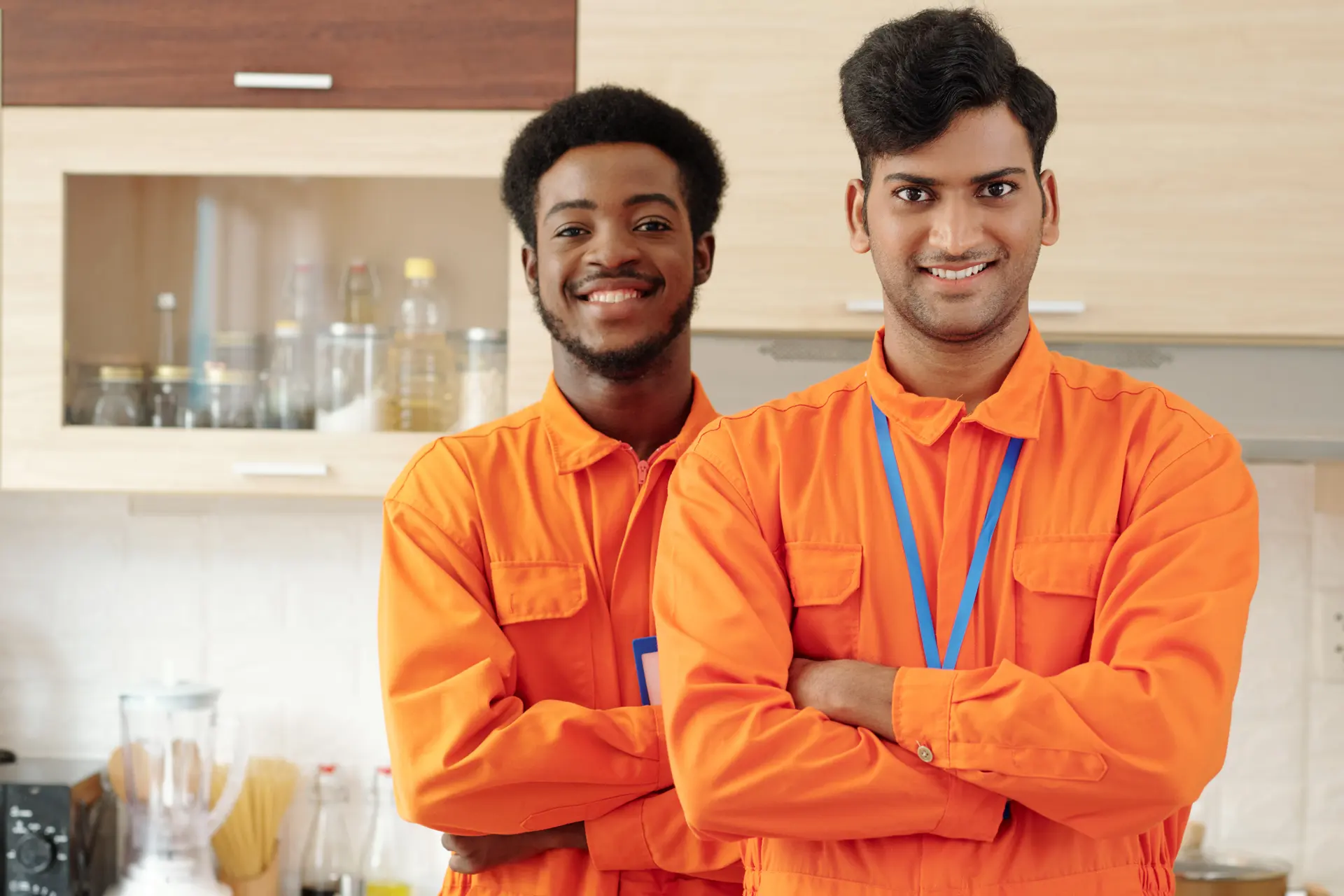 Two tradespeople in orange work shirts smiling with their arms folded