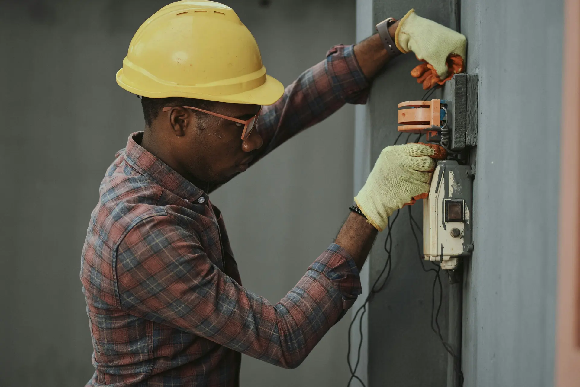 An electrician in a hard hat working on an outdoor electricity meter