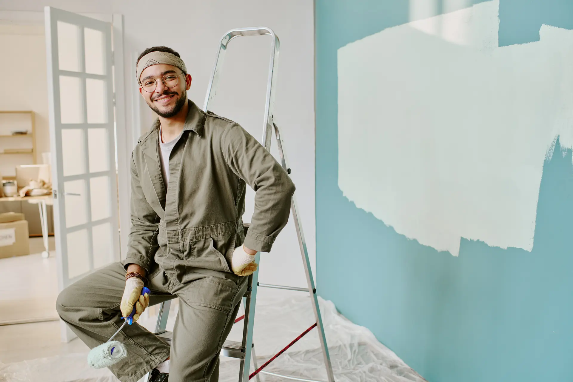 A painter on a stepladder smiling beside a half-painted wall