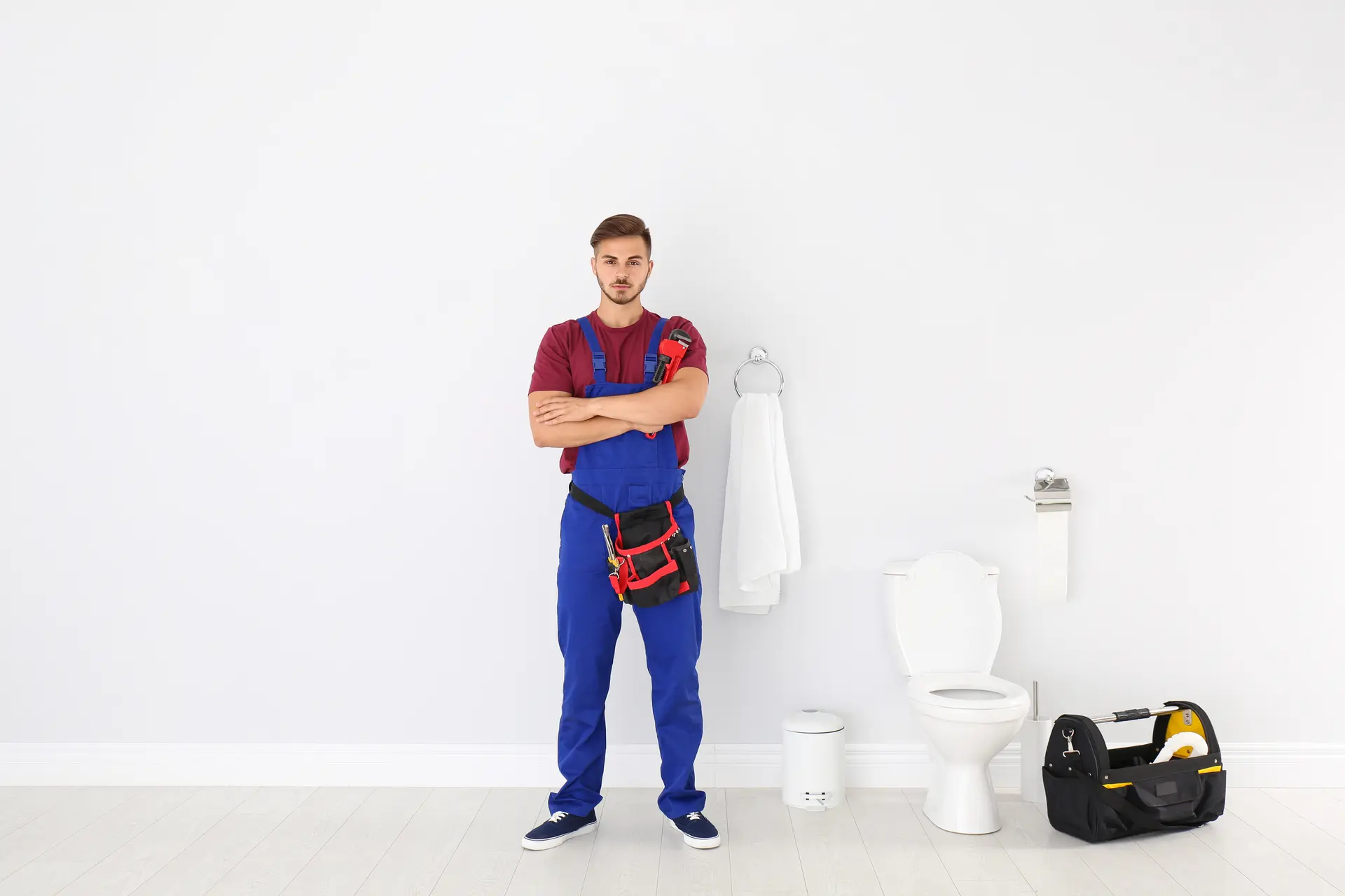 A plumber with a tool belt standing in a bright white bathroom