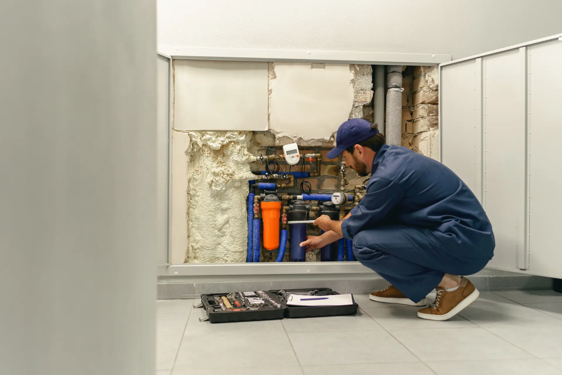 A plumber working on pipework inside a utility cupboard