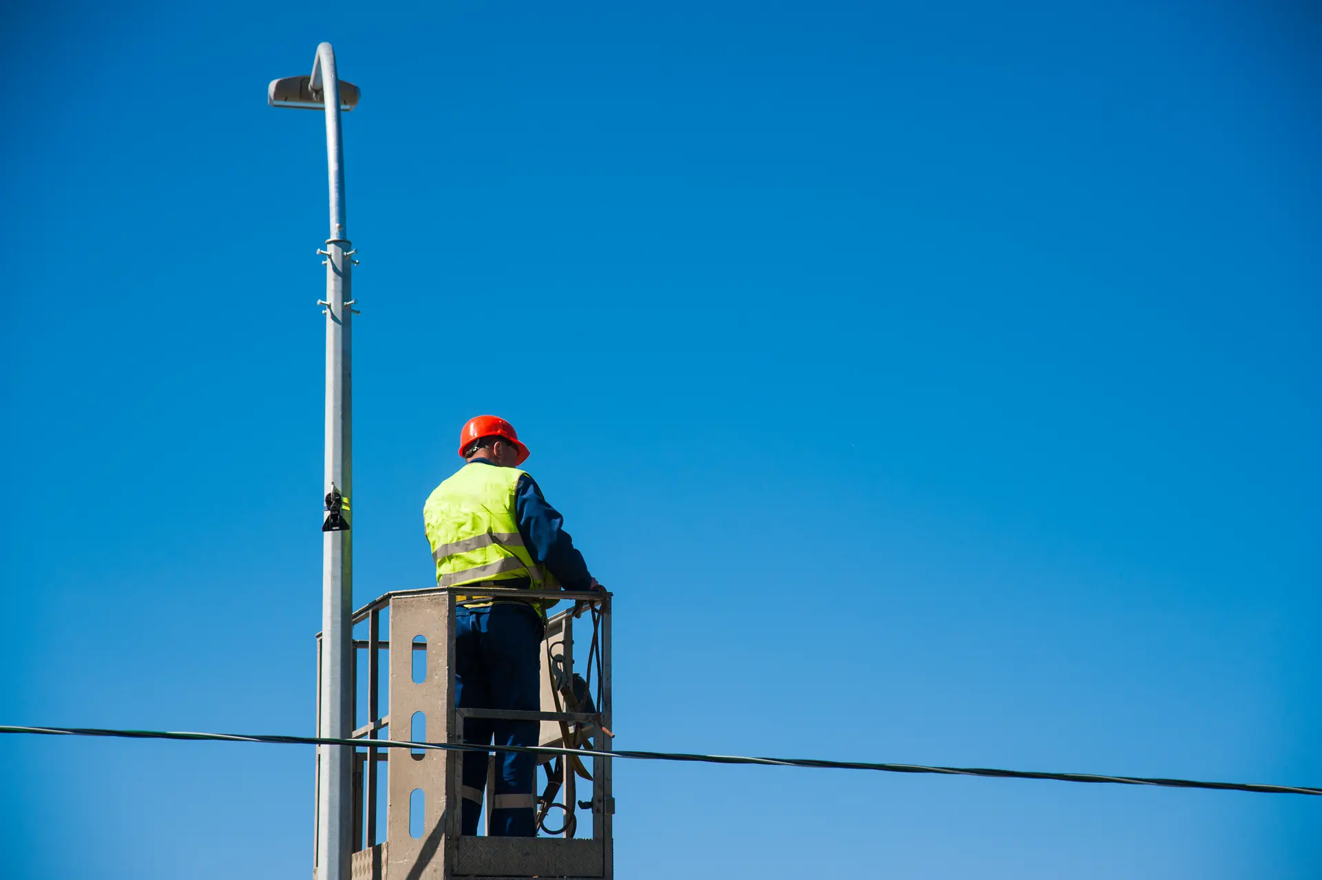 A worker in a cherry picker servicing a street light against a blue sky