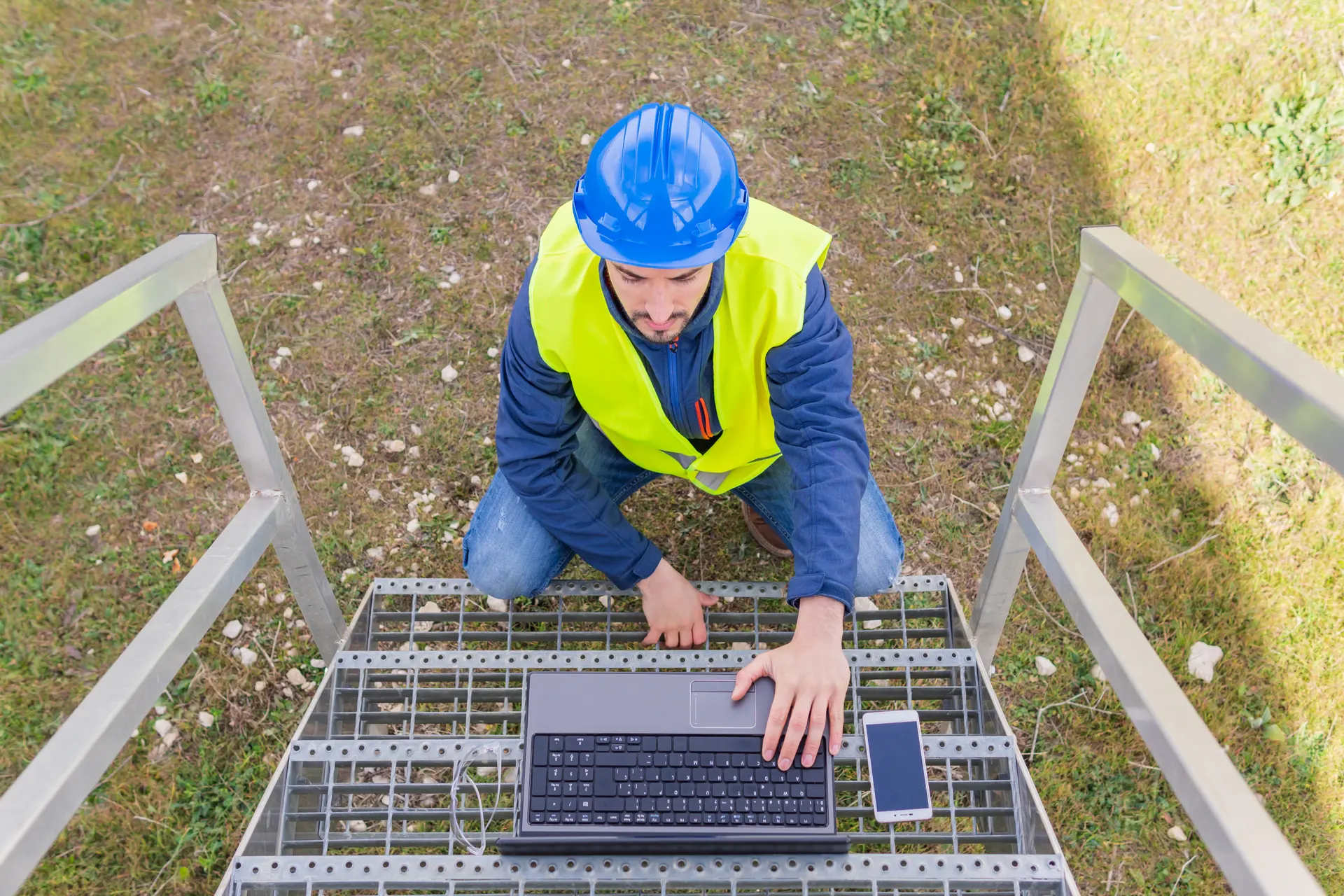 A supervisor using a laptop on an outdoor staircase at a site